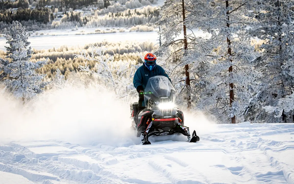 Un conducteur de motoneige soulevant la neige sur une piste damée au-dessus d'une forêt givrée