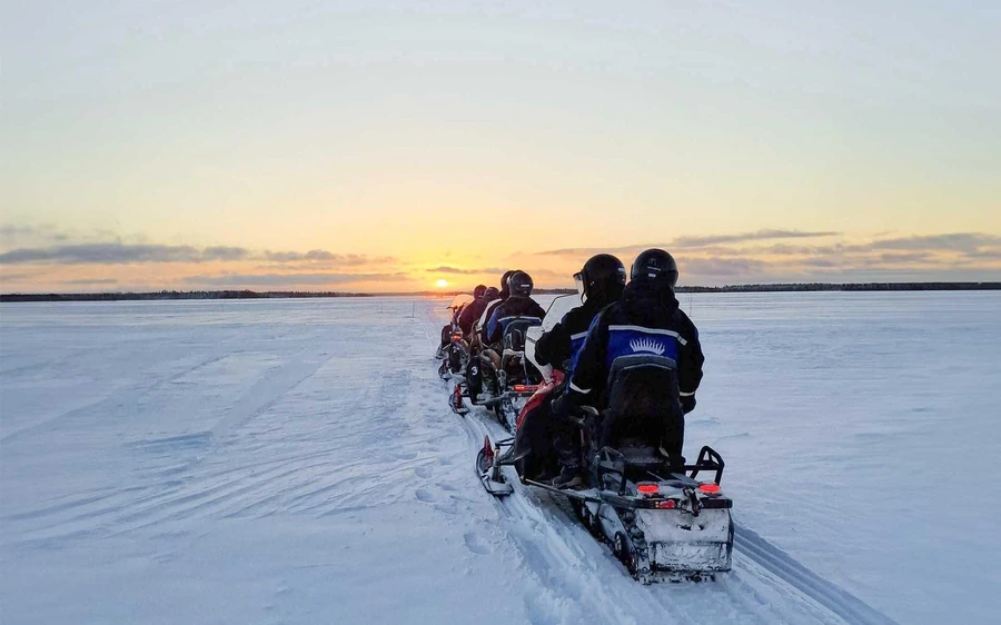 Une file de motoneiges traversant la neige à perte de vue au coucher du soleil
