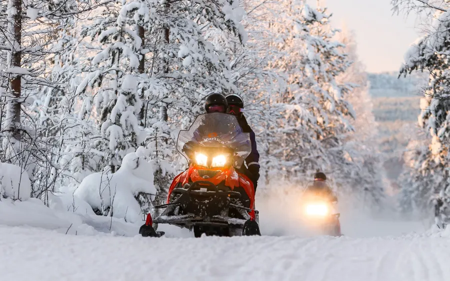 Une motoneige phares allumés entre des arbres lourdement chargés de neige